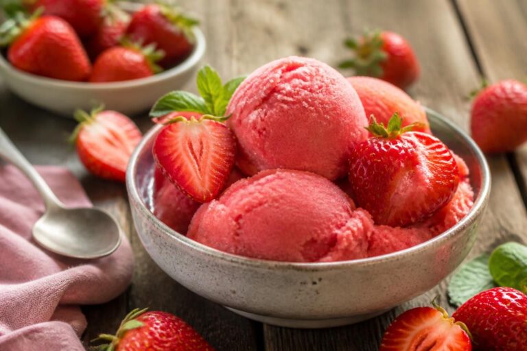 Cremiges Erdbeer-Sorbet ohne Eismaschine in einer Gefrierdose, garniert mit frischen Erdbeeren und Minzblättern