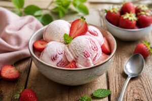 Erdbeer-Joghurt-Eis in einer Schüssel, garniert mit frischen Erdbeeren und einem Holzlöffel, von oben fotografiert