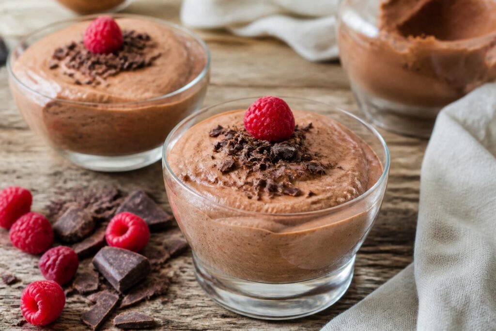 Vegane Schokoladen-Mousse ohne Sahne und Ei mit Aquafaba, serviert in Glasschalen mit frischen Beeren und Kakaopulver, fotografiert von oben auf hellem Holzhintergrund