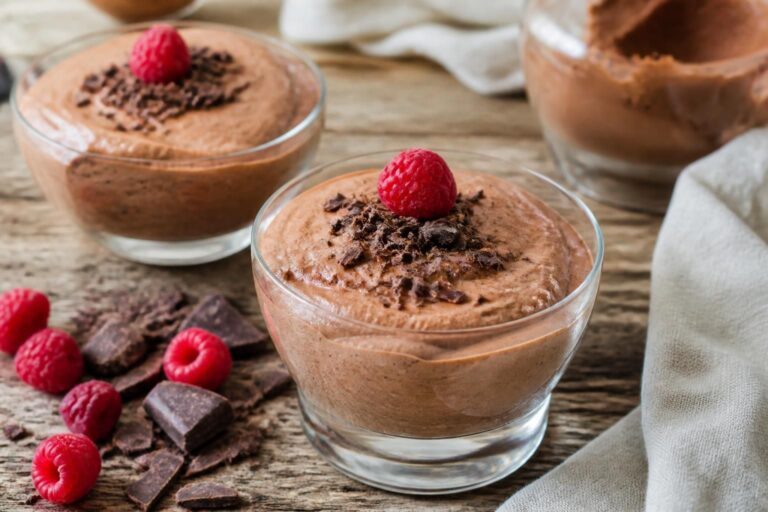 Vegane Schokoladen-Mousse ohne Sahne und Ei mit Aquafaba, serviert in Glasschalen mit frischen Beeren und Kakaopulver, fotografiert von oben auf hellem Holzhintergrund