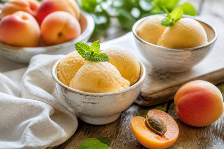 Aprikosen-Joghurt-Sorbet ohne Eismaschine in einer weißen Schüssel, garniert mit frischen Aprikosenspalten und Minzblättern