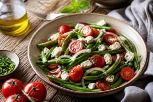Sommerlicher Bohnensalat mit Cherrytomaten und Feta in einer weißen Schüssel, beträufelt mit Olivenöl-Balsamico-Dressing, garniert mit frischen Kräutern