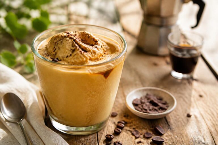 Frozen Cappuccino ohne Eismaschine im hohen Glas mit cremiger Kaffeeschicht, Eiswürfeln und Kakaopulver on top, von oben fotografiert