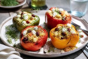Gefüllte Paprika vom Grill mit Feta und Couscous auf einem Holzbrett, garniert mit frischer Petersilie und Zitronenspalten