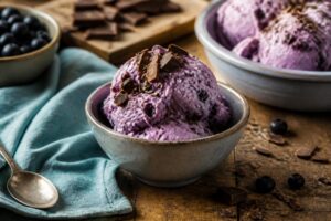 Selbstgemachtes Heidelbeer-Stracciatella-Eis ohne Eismaschine in einer weißen Schale, garniert mit frischen Heidelbeeren und dunklen Schokoladenstückchen