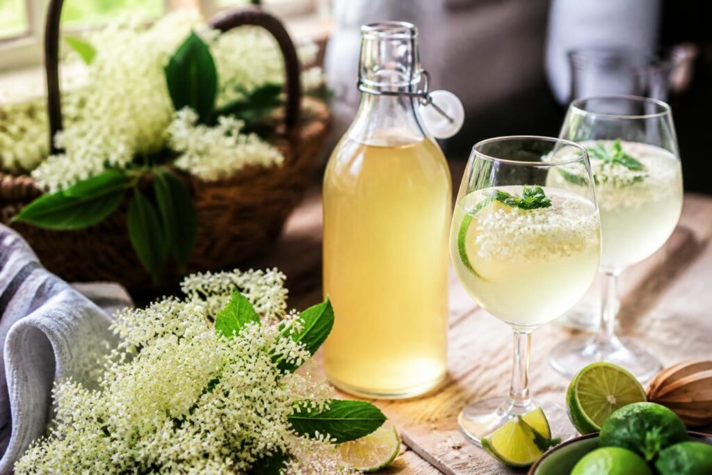 Selbstgemachter Holunderblütensirup in einer Glasflasche, umgeben von frischen Holunderblütendolden und Zitronenscheiben auf einem Holztisch