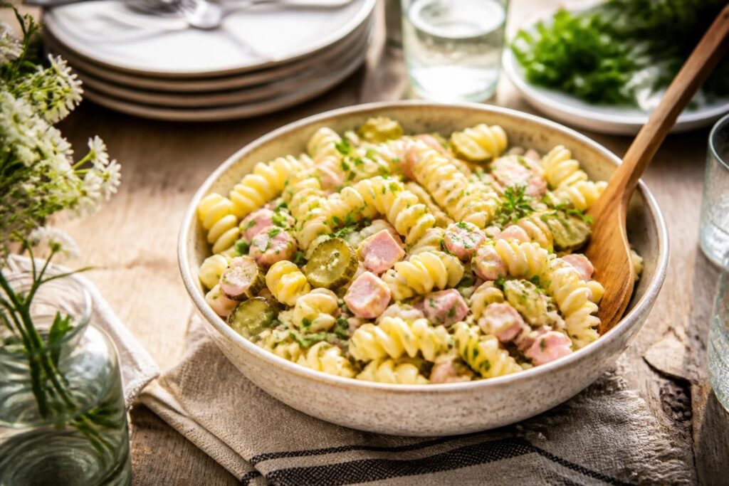 Schwedischer Nudelsalat mit Sweet-Chili-Dressing, Mais, Gurke und frischer Petersilie in einer weißen Schüssel