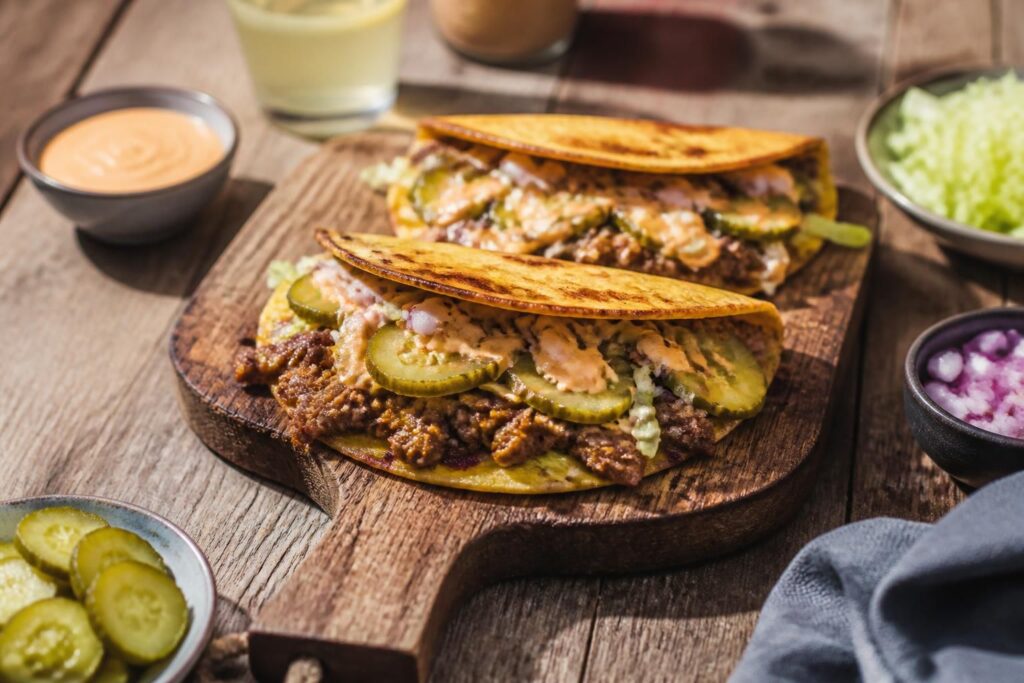 Smash Burger Tacos auf einem Holzbrett: gefaltete Weizen-Tortillas mit Smash-Patty, geschmolzenem Cheddar, roten Zwiebeln und Burgersauce