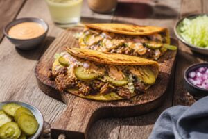 Smash Burger Tacos auf einem Holzbrett: gefaltete Weizen-Tortillas mit Smash-Patty, geschmolzenem Cheddar, roten Zwiebeln und Burgersauce