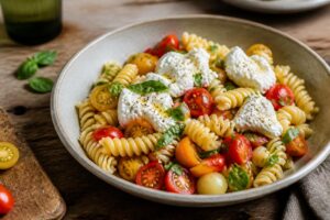 Sommer-Pasta mit Burrata und Kirschtomaten in einer weißen Schüssel, garniert mit frischem Basilikum und Olivenöl