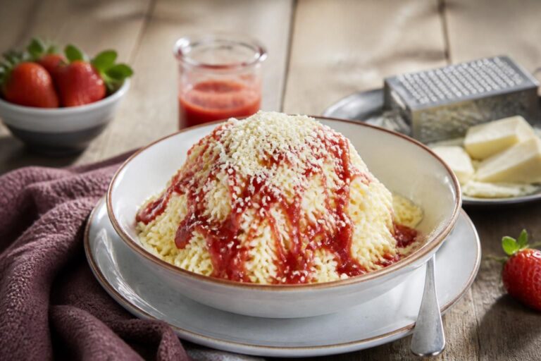 Selbstgemachtes Spaghettieis in einer weißen Schüssel: Vanilleeis-Spaghetti mit Erdbeersauce und weißen Schokoladenraspeln