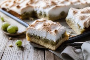Stachelbeer-Baiser-Kuchen vom Blech mit goldbrauner Baiserhaube und frischen grünen Stachelbeeren auf einem hellen Backblech